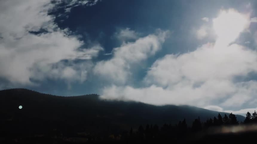 Clouds move over forested mountains