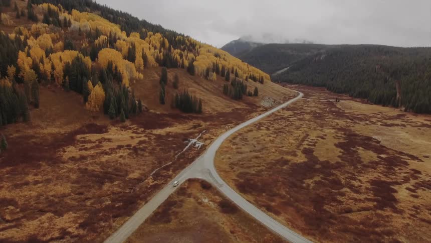 Aerial panorama of a road amidst a mountainous landscape and forests on a cloudy day