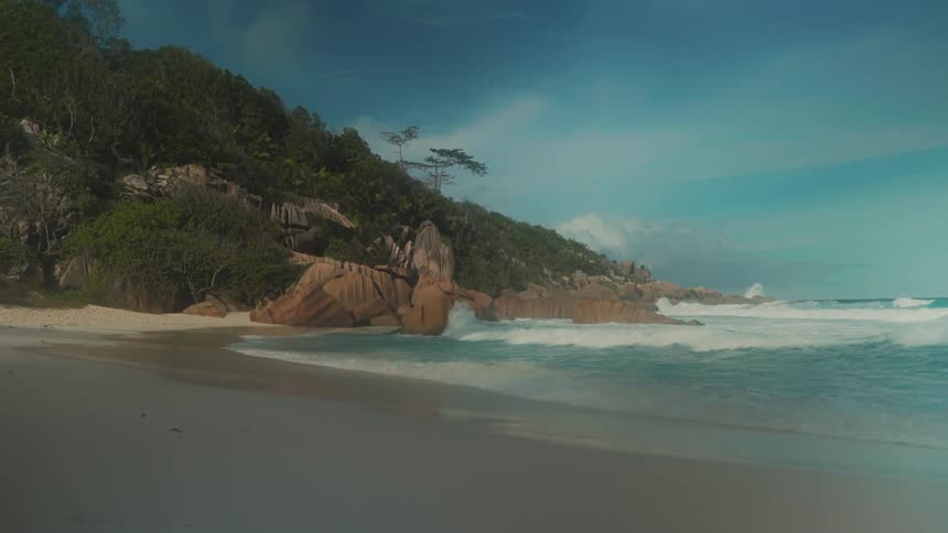 Ocean waves crash on a shore with a large moss covered rock
