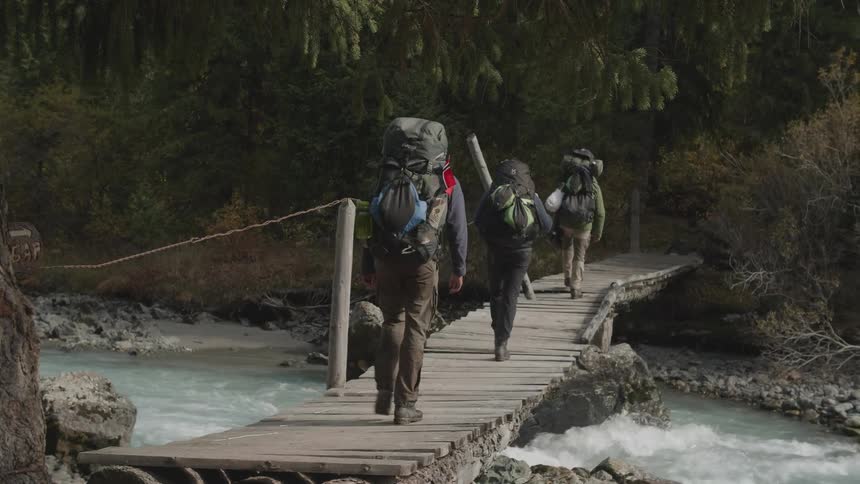 Three people crossing a small wooden bridge over a river