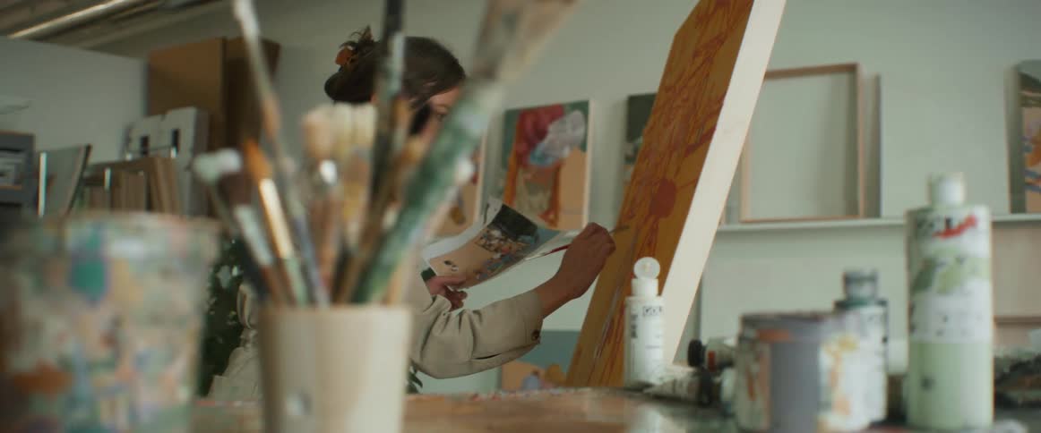 Woman painting on a canvas holding a reference image with the other hand