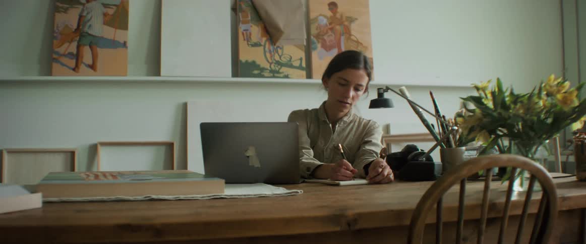 Woman writes on a notebook while seated in an art studio at midday