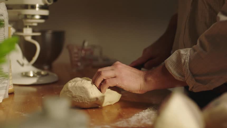 Man uses a kitchen knife to cut dough in the kitchen