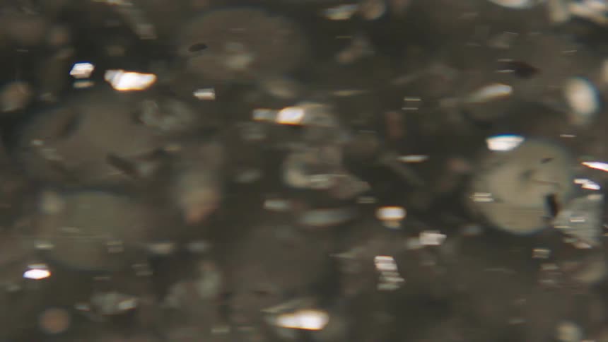Liquid spinning with metallic confetti in abstract slow motion