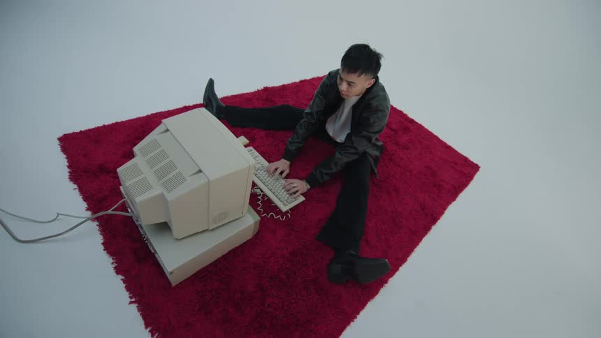 Man uses desktop computer sitting on red rug