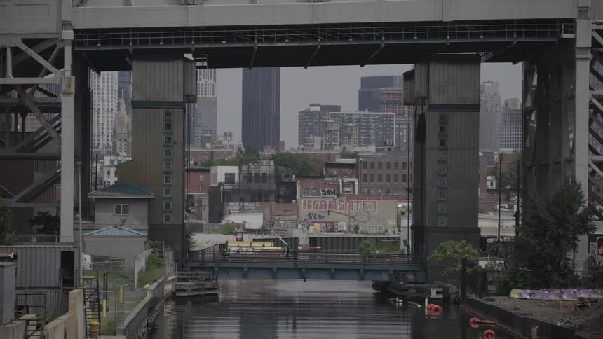 Two people walking along a walkway under a bridge and there is a river