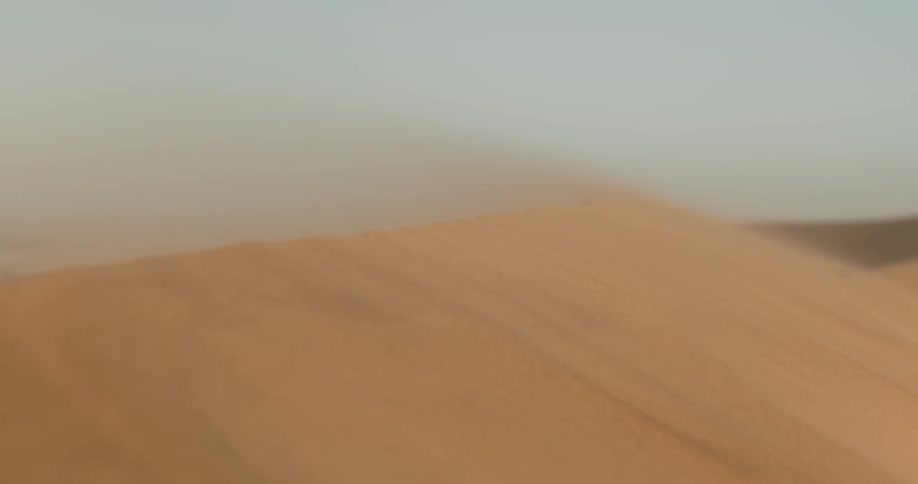 Wind blows sand over a dune in the desert