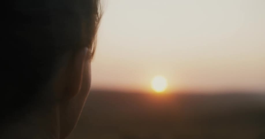 A woman looking at the sunset as the wind moves her hair