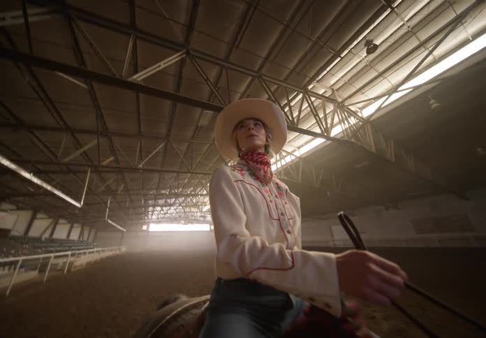 A woman on horseback walking through a dirt arena