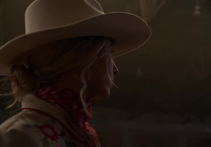 A woman in a cowboy hat is looking around looking for something and its dark