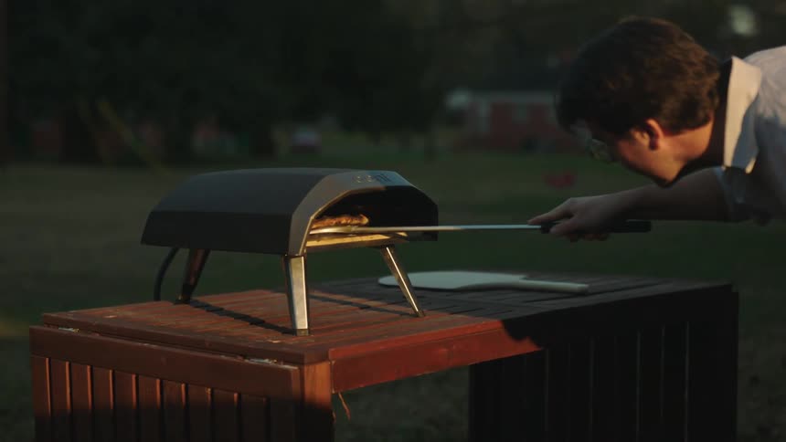 Man cooks a pizza on a small outdoors oven
