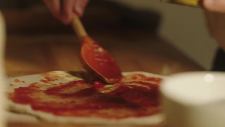 Man spread sauce on a pizza indoor