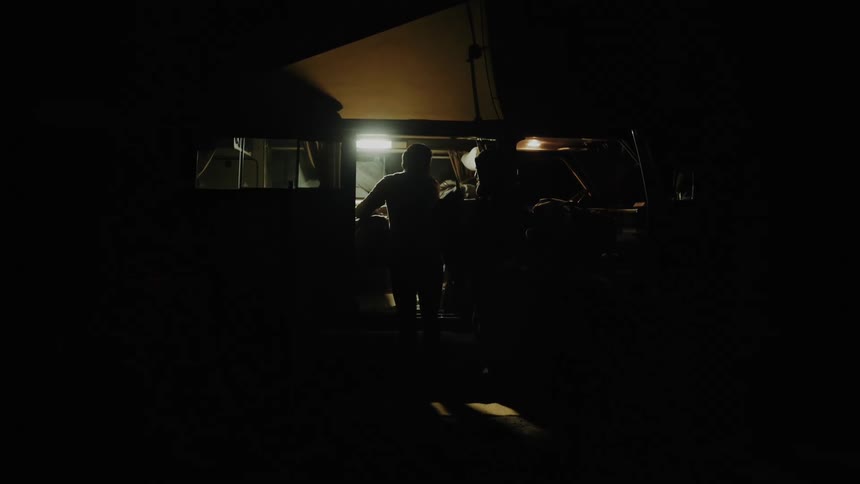 Two people loading objects into a van at night