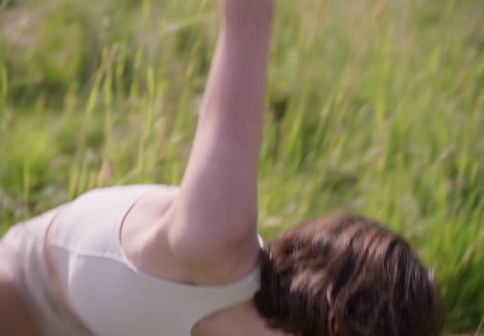 A woman stands in a grass field and performs with her arms