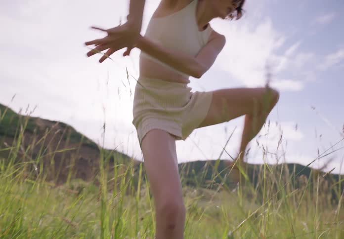 Woman with bob hairstyle a white shirt and shorts dances on green grass in the field
