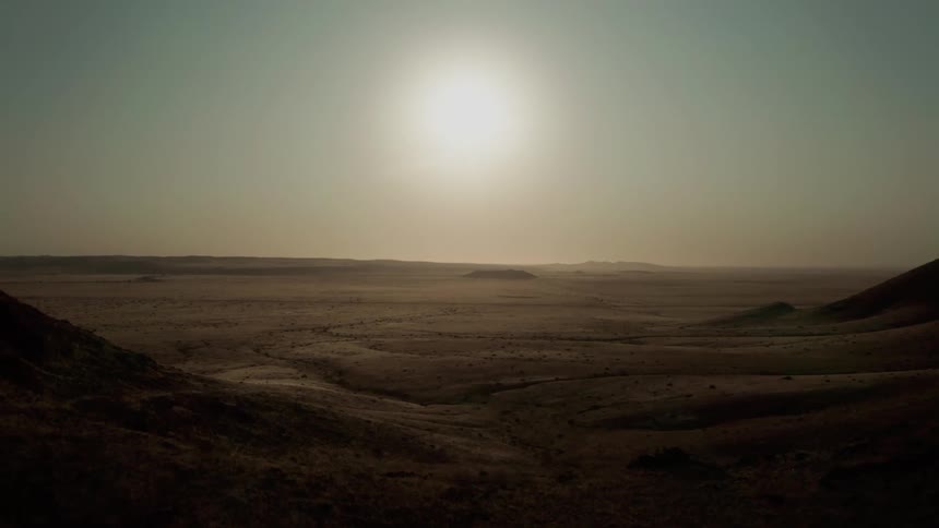 Panorama of a landscape with mountains and a desert area with the sun shining in a cloudless blue sky