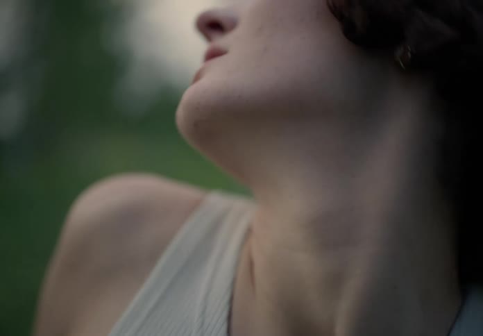 A woman with a bob hairstyle and a white shirt joyfully dances in a green field