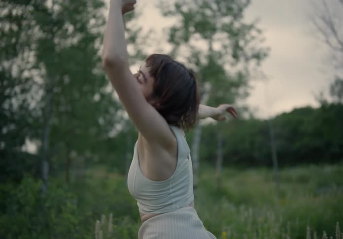 Woman dancing gracefully in the midst of nature facing away under the daylight