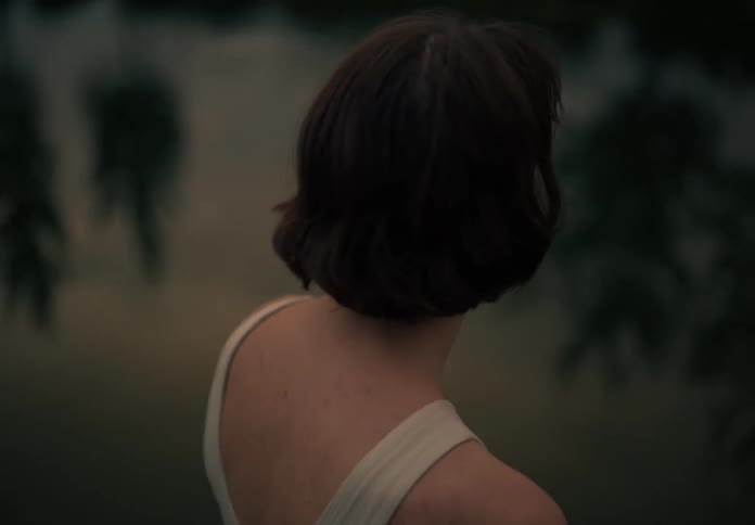 Woman with bob hairstyle and a white dress stands by lake at dusk