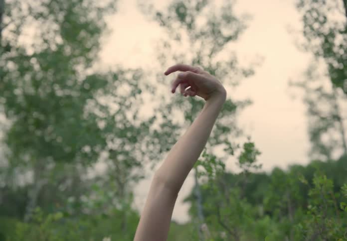A woman dancing with her arms up in a forest