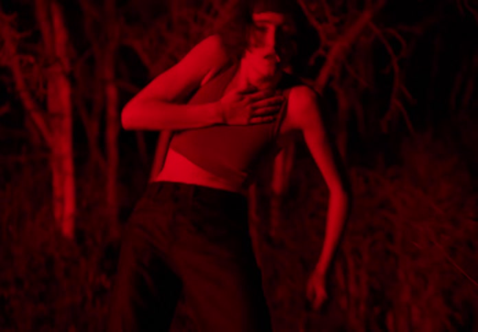 Young thin woman dances under red lights outdoors