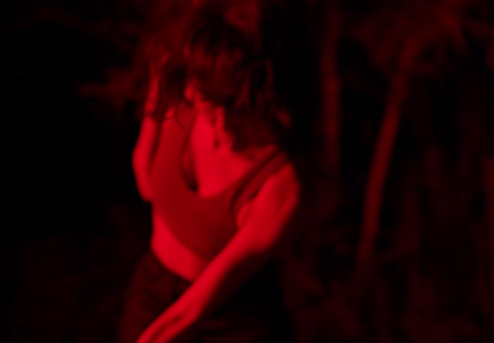 Woman dancing scenically in the middle of a forest at night with red lighting