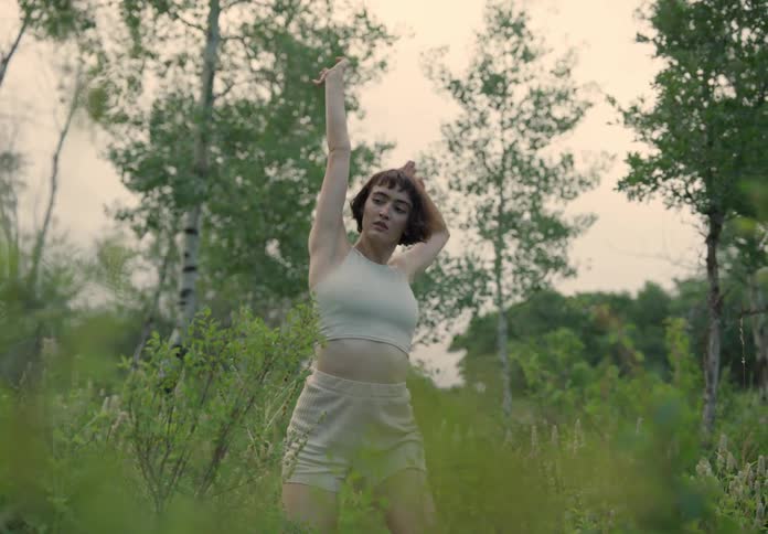 Young thin woman dances stretching on a field of green grass