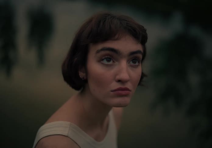 Woman with a bob hair and white shirt looks around by a serene lake