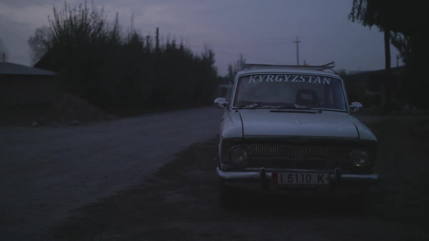 Old white car stands by dirt road