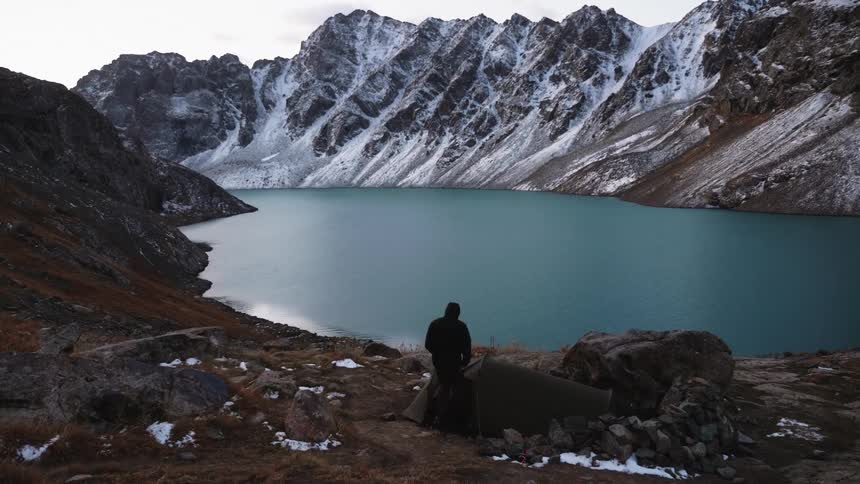 A man camps by a tent near ala kul lake surrounded by the serenity of nature