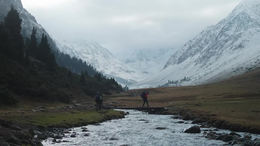 Three people carrying heavy backpacks walking over a stream at daytime