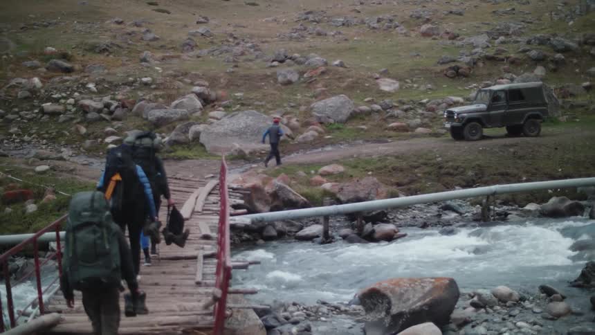 People walking across a small wooden bridge over a flowing river seen from behind