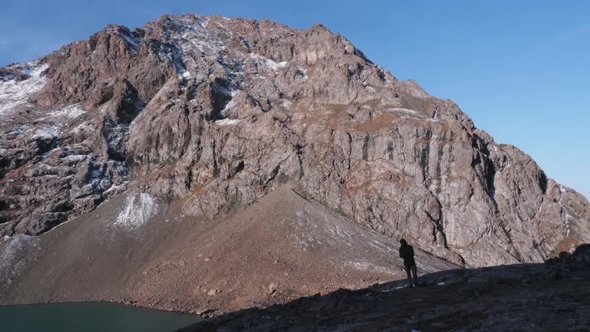 A man standing below a mountain on a sunny day during fall