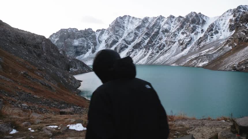 A person on the shore of a lake surrounded by icy mountains