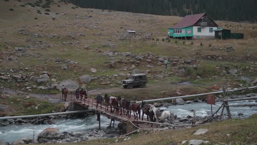 Men crossing a small bridge over a river with several horses