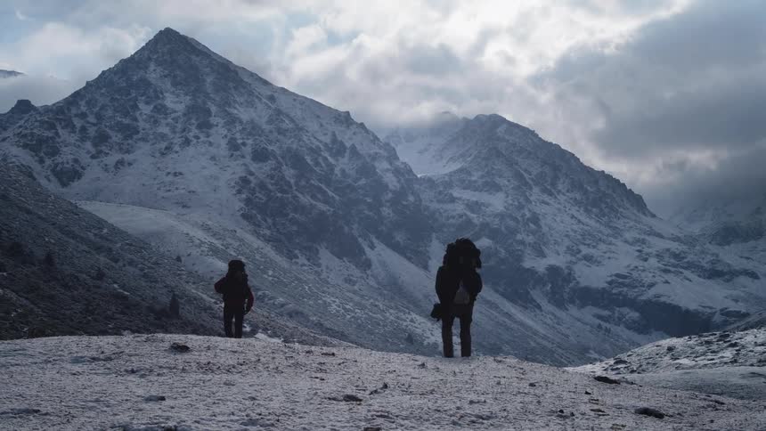 Two people walking away their backs to the camera through snowcovered mountains on a cloudy day