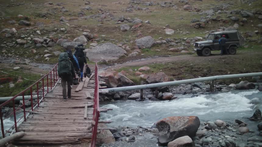 People crossing a river under a small wooden bridge