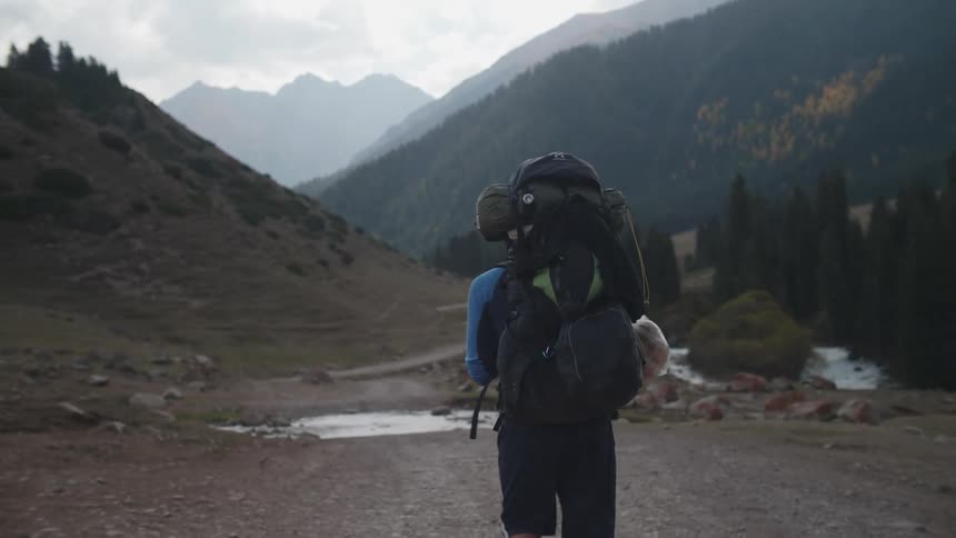 A man with a large backpack walking through a landscape of plains and mountains