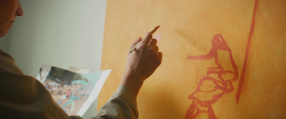 Woman painting a picture while looking at an image in her other hand