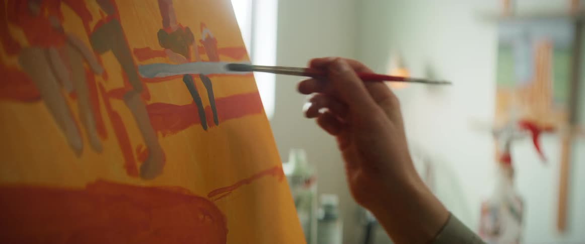 An artist paints an orange and yellow scene on a canvas