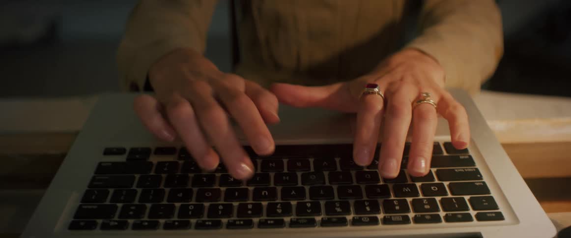 Hands of a lady typing on a laptop while seated indoor