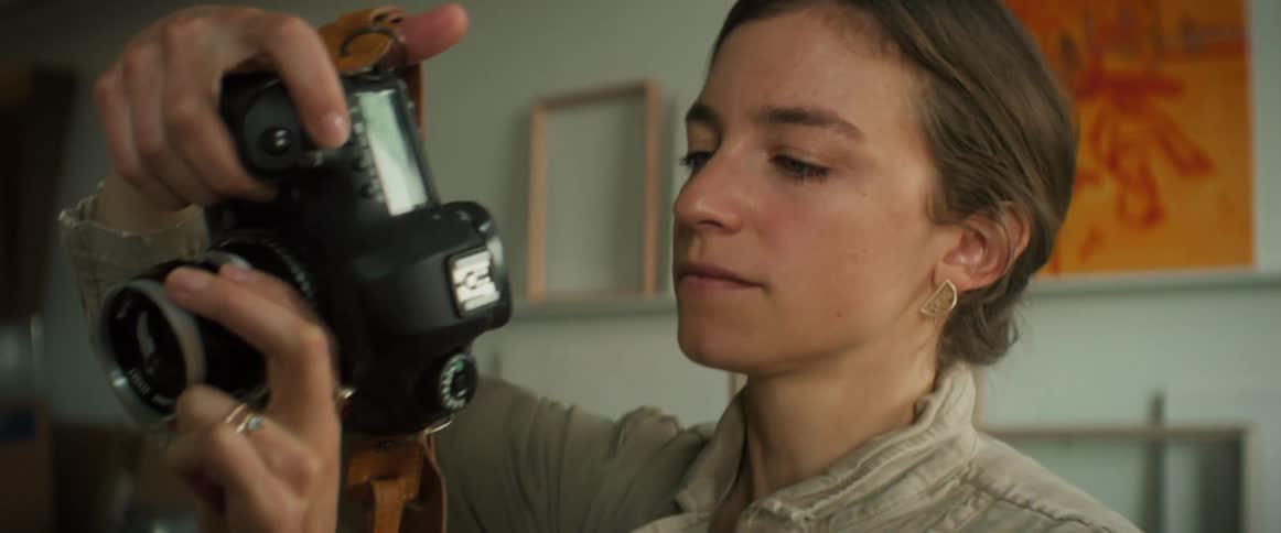 A young woman holds a camera up to her eye and makes adjustments to it