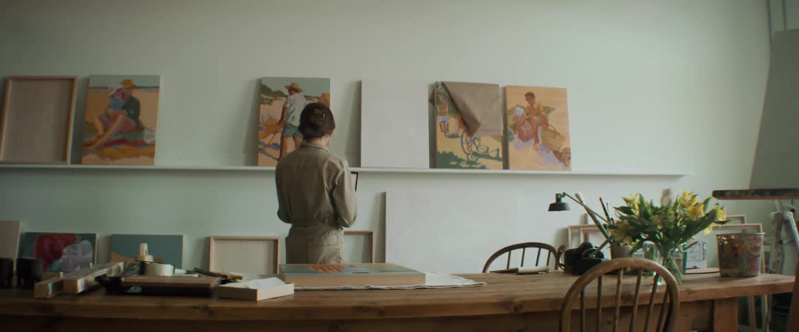 Woman sitting with her back to the camera using her laptop and looking at artworks on the wall in a room