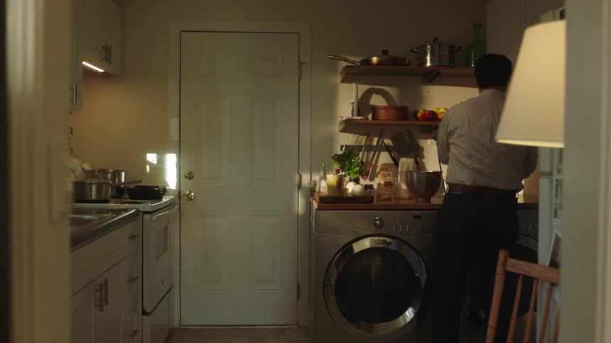A man is in an environment with a kitchen and laundry room and places objects from one location to another
