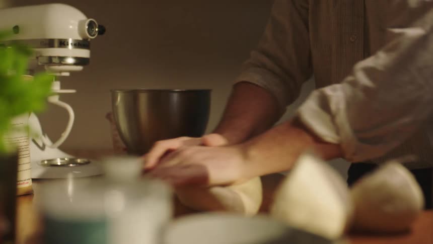 Closeup of a man in a shirt kneading dough with focused determination