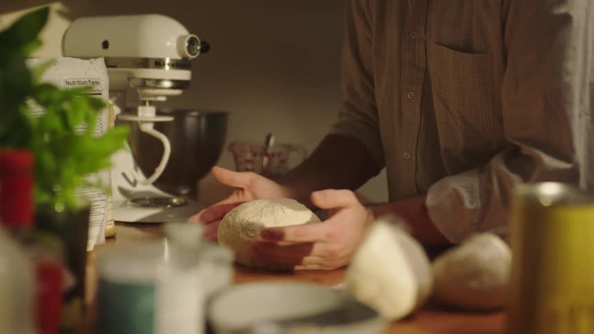 Man wearing a shirt kneads a dough in the kitchen