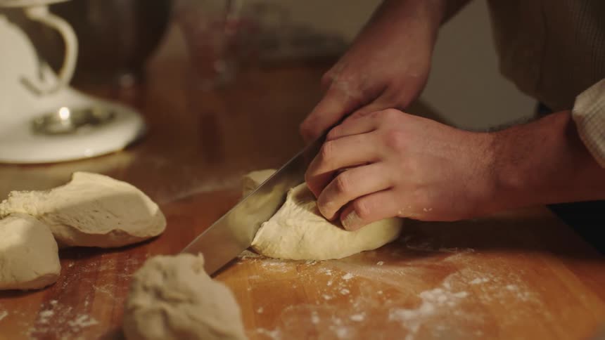 Man cuts up dough with a knife in the kitchen