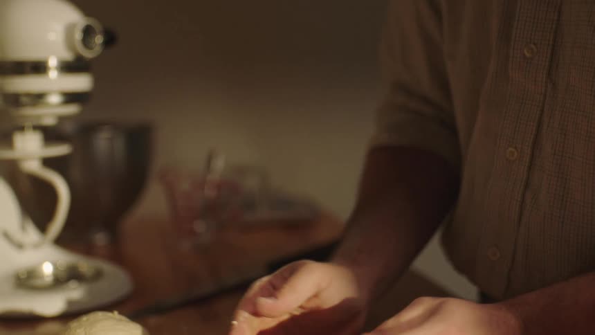 A person is kneading bread dough and placing it on a wooden table