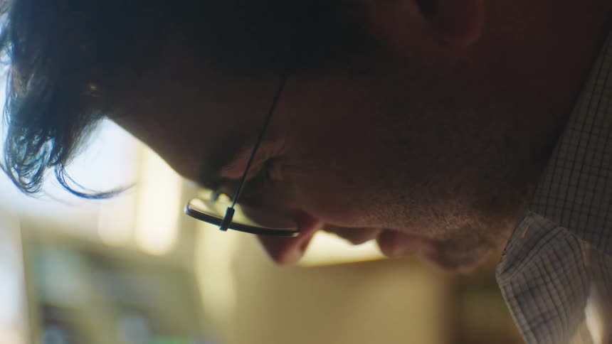 Closeup of a mans face wearing glasses and a shirt looking down and smiling