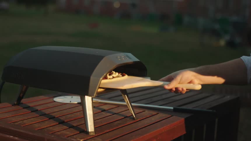 Man placing a pizza to bake in an outdoor oven